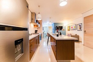 Une cuisine moderne dotée d’un distributeur d’eau intégré, d’appareils électroménagers en acier inoxydable et de luminaires suspendus.