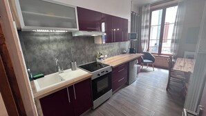 A modern kitchen with a built-in oven, a sink, and a microwave. There is a dining area with a table and chairs visible through a window. - Apartment 2/4/6 pers. HYPER CENTRE, quiet (dead end) with PARKING, linen provided (Cauterets)