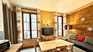 A cozy room with a wooden table and chairs, a television, and a sofa with cushions. - Apartment 2/4/6 pers. HYPER CENTRE, quiet (dead end) with PARKING, linen provided (Cauterets)