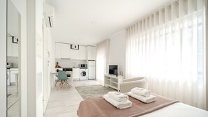 Une chambre d’hôtel moderne avec un grand lit, une télévision et, au fond, une petite cuisine.
