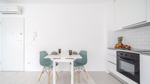Une cuisine moderne avec des meubles blancs, un four encastré et un coin repas comprenant une table blanche et deux chaises de couleur turquoise.