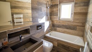Ein modernes Badezimmer mit Holzwandgestaltung, einer Badewanne, einem Waschbecken und einem Fenster für natürliches Licht.
