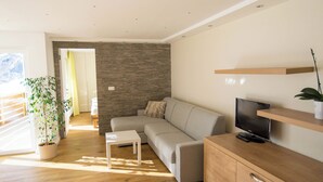 Ein modernes Wohnzimmer mit einer Couch, einem Fernseher, einem Holzschrank und einem Blumentopf.