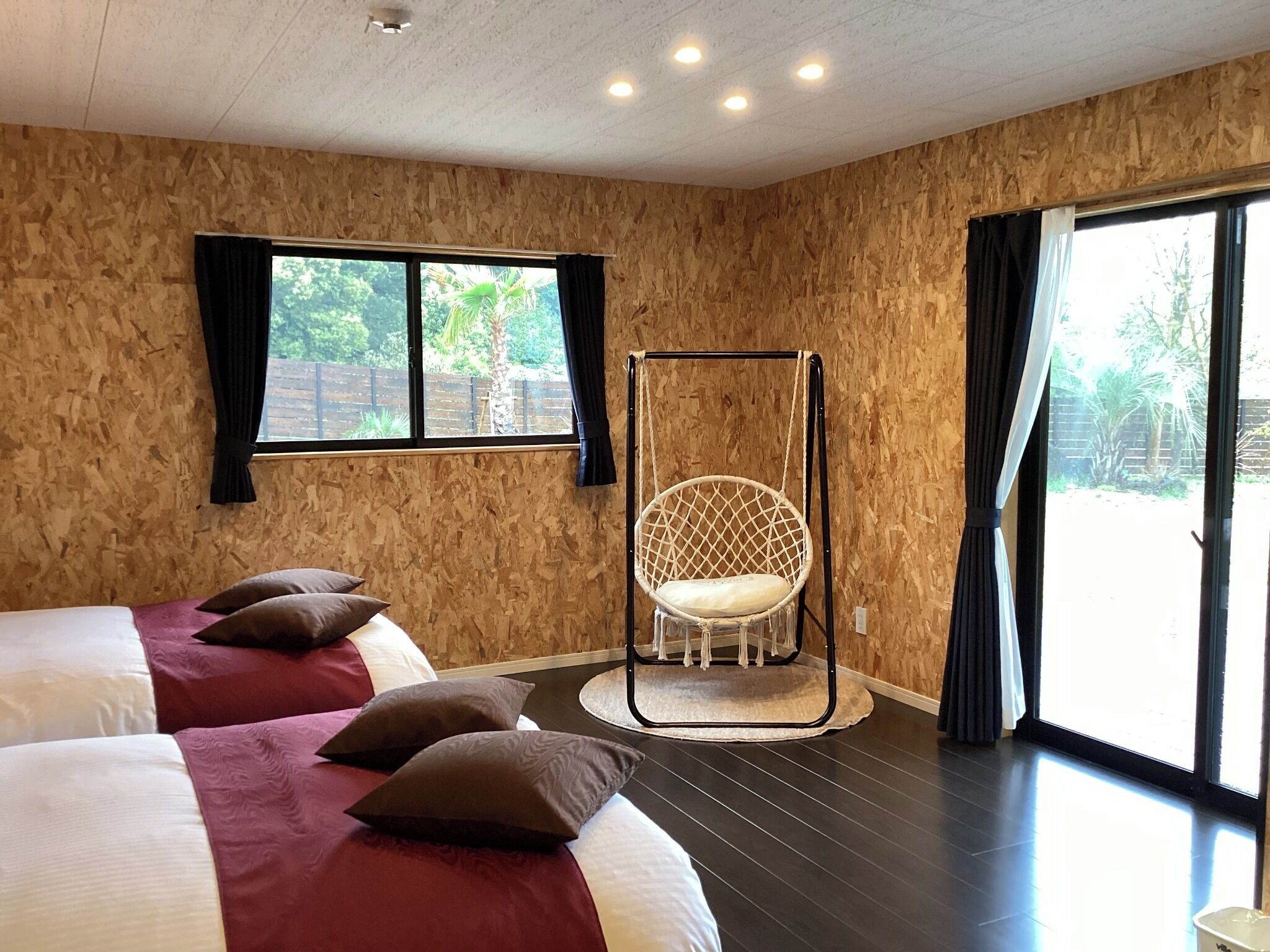 A room with two beds, a hanging chair, a window, and a view of the outdoors.