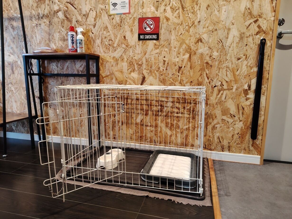 A pet cage with a litter box inside, a no smoking sign, and a small table with cleaning supplies.