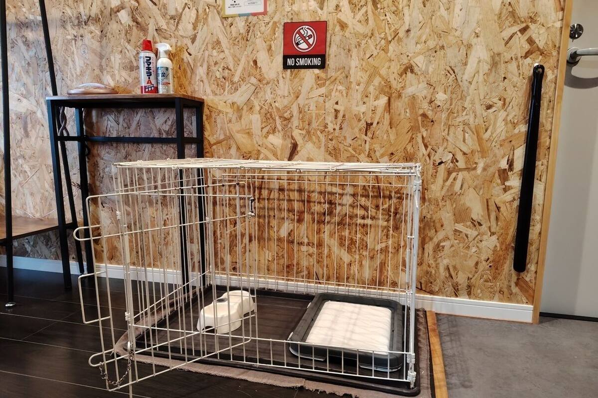 A pet cage with a litter box inside, a no smoking sign, and a small table with cleaning supplies.