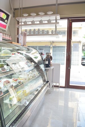 Vitrina de pastelería con varios productos horneados, una máquina de café y un mostrador con un menú.
