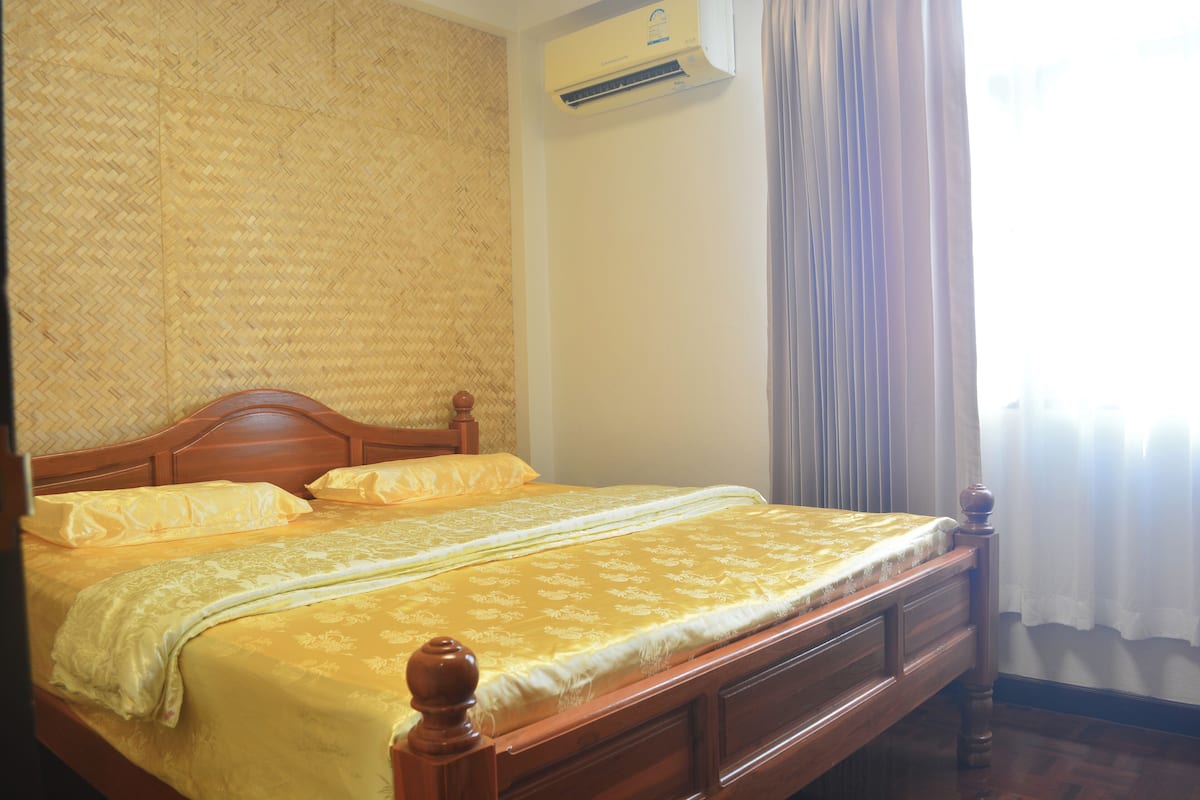 A bed with a wooden frame, a yellow bedspread, and a white pillow.