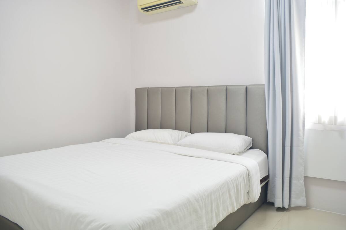 A neatly made bed with a grey headboard in a simple, clean room.