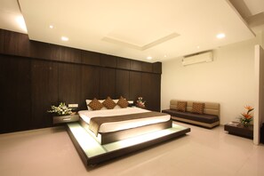 A modern bedroom with a large bed, a sofa, a nightstand, and an air conditioning unit.