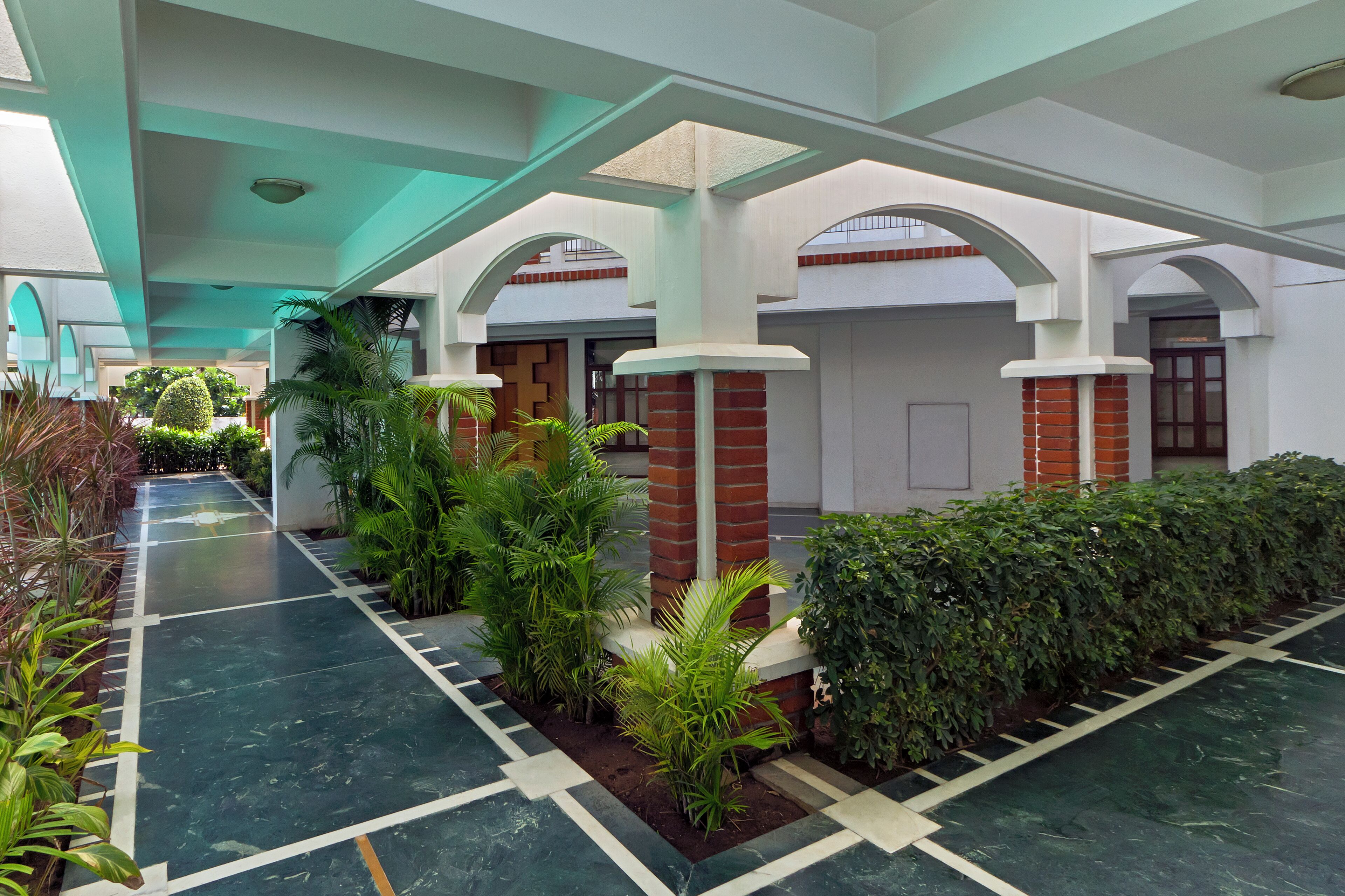 A spacious indoor area with a tiled floor, green plants, and white pillars.