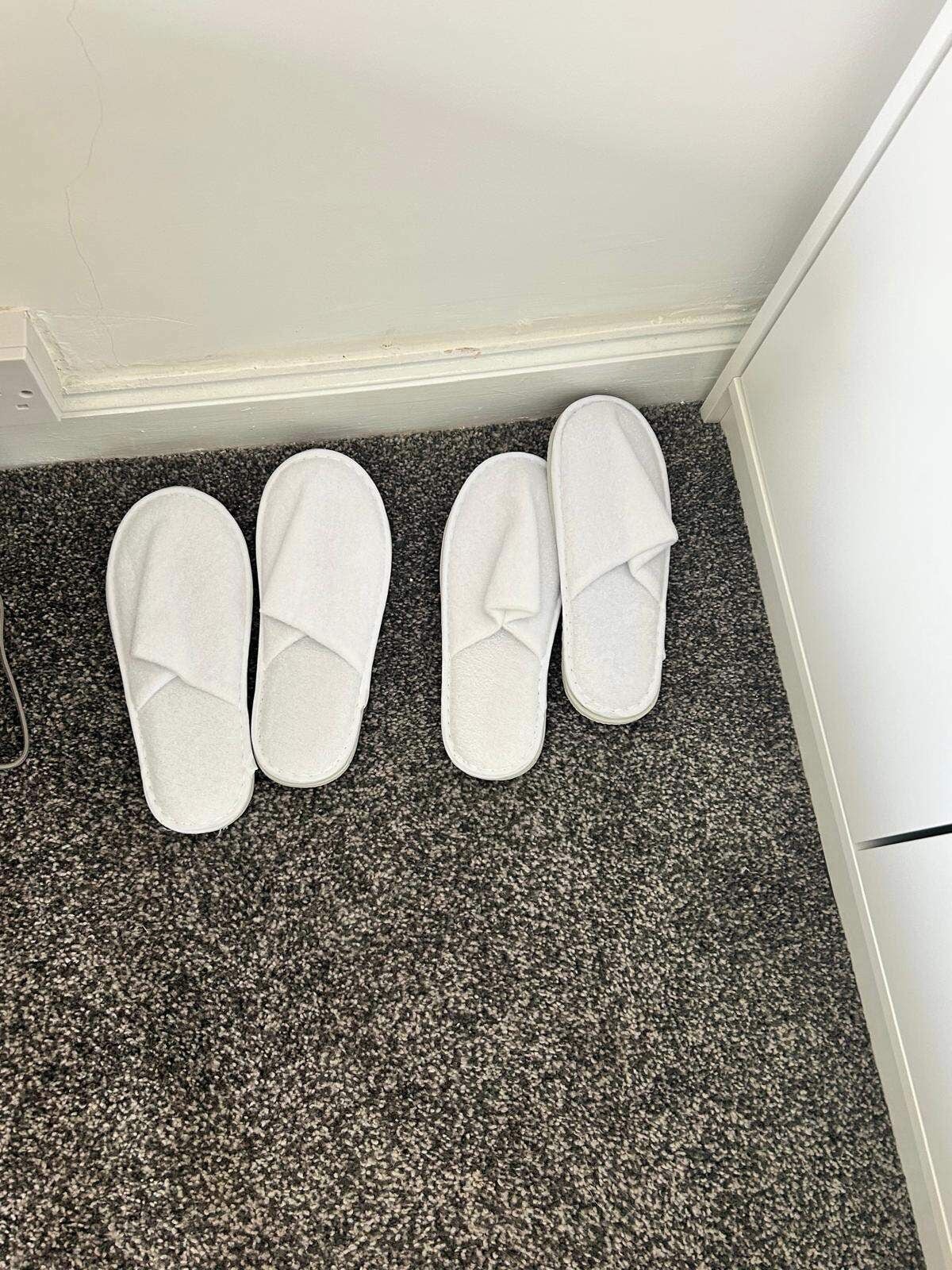 A pair of white slippers on a speckled carpet near a white wall.