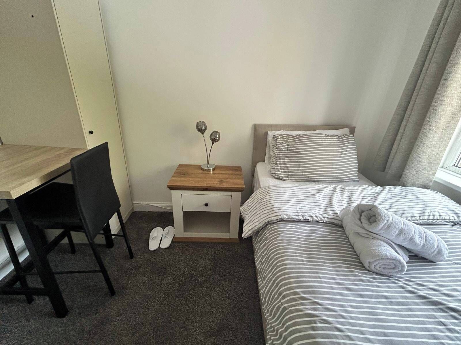 Una habitación de hotel con cama, mesita de noche, silla y escritorio.