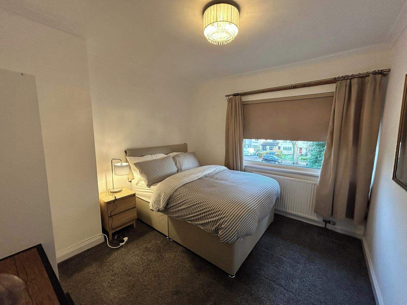 A neatly arranged bedroom with a bed, bedside table, lamp, and a window with curtains.