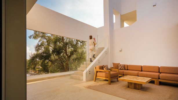 Ein modernes Interieur mit einer Treppe, einem Holzsofa und einem großen Fenster mit Blick auf Bäume.
