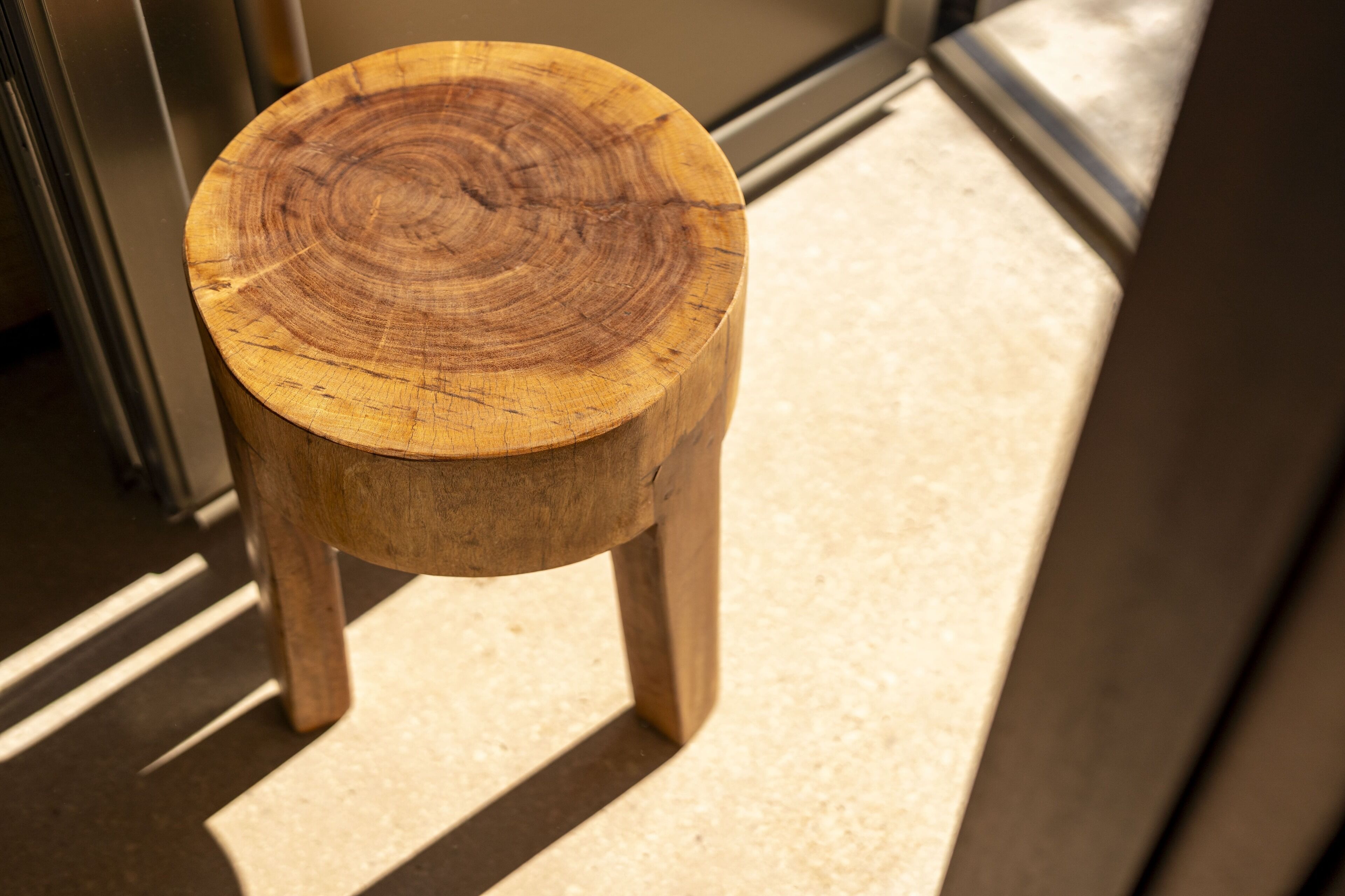 A wooden stool with a visible tree ring pattern, placed on a tiled floor.