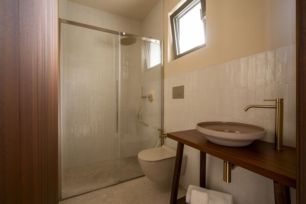 Un baño con ducha de vidrio, inodoro y tocador de madera con lavamanos.