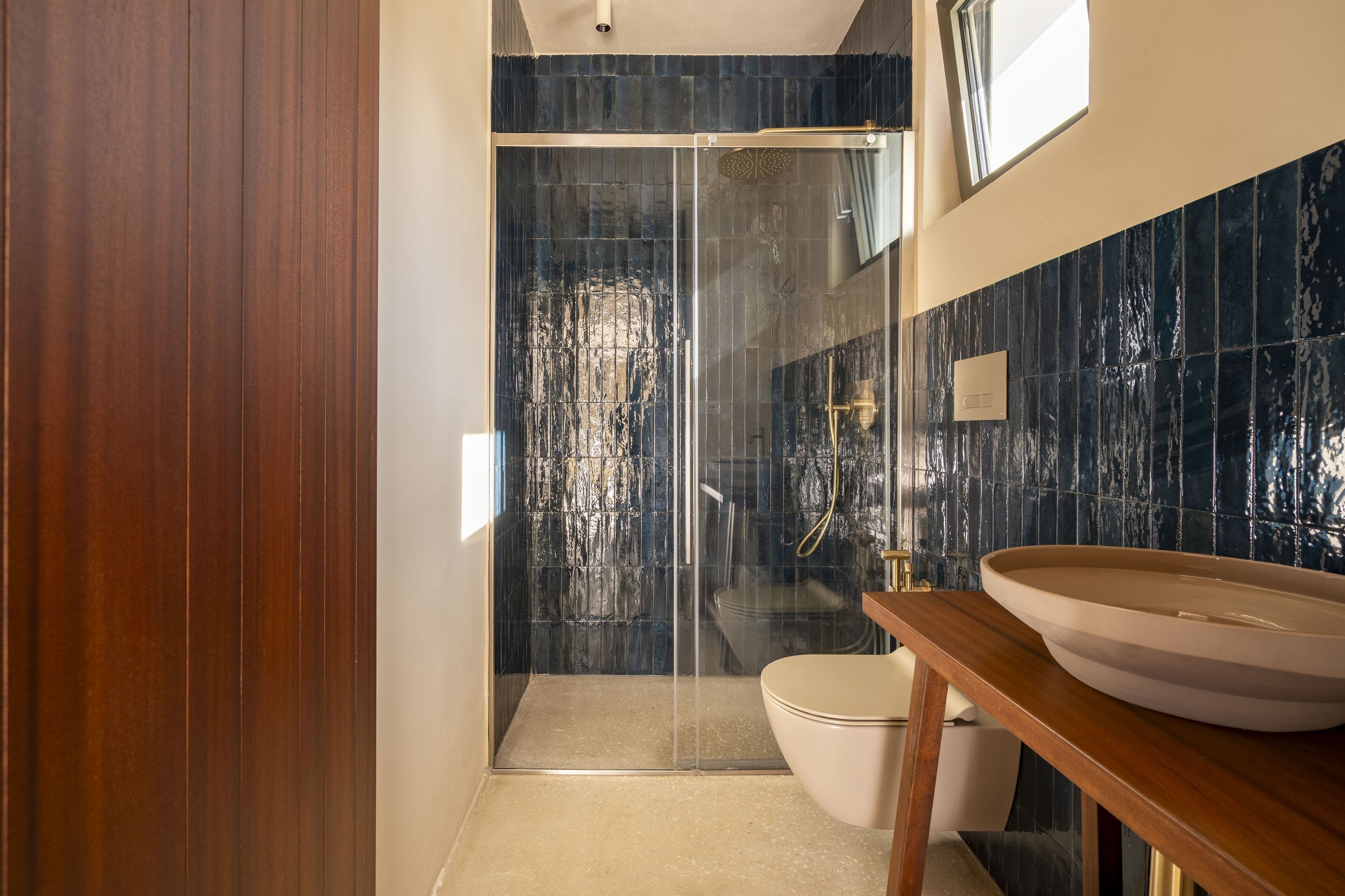 A modern bathroom with a glass-enclosed shower, a wooden vanity, and a marble-tiled wall.