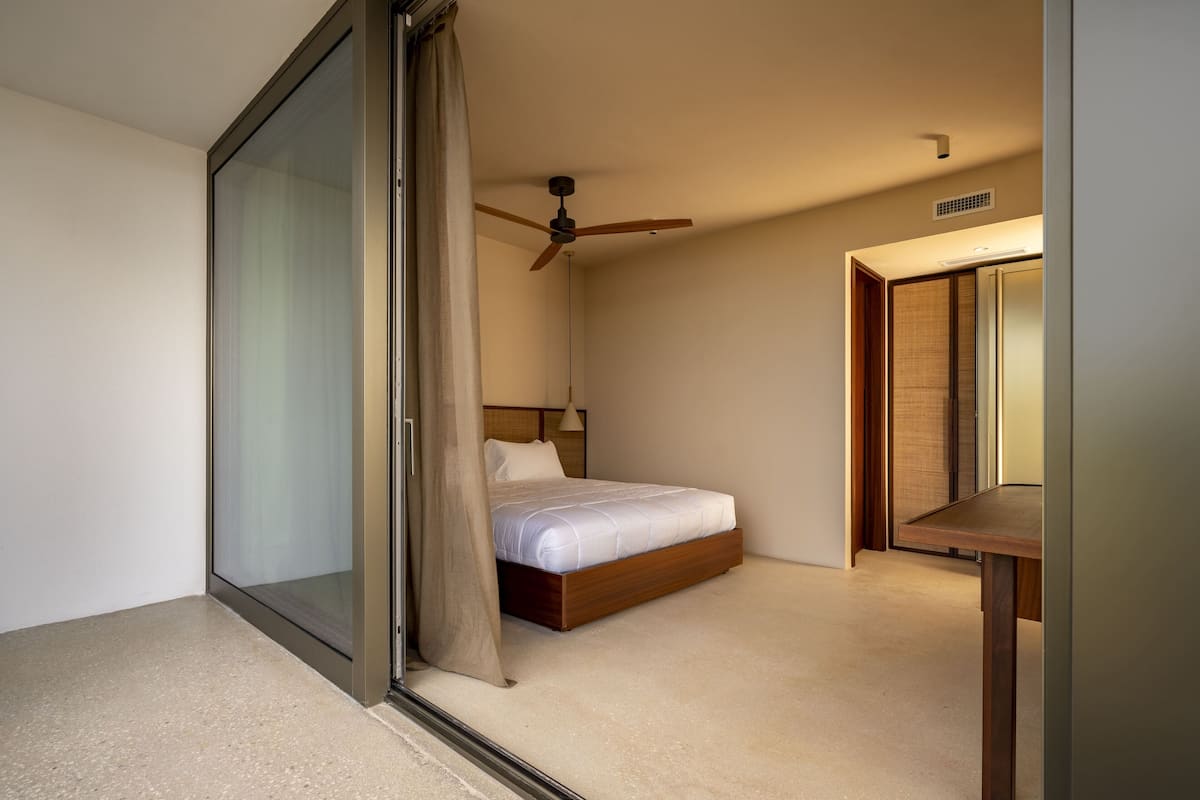 A bedroom with a bed, a ceiling fan, a bedside table, and a sliding door.