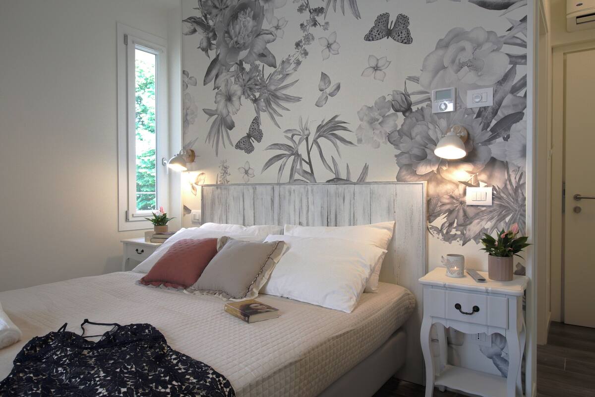 Ein Schlafzimmer mit einem Bett, Nachttischen, einem Fenster und einer Wand mit Blumenmuster.