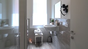 Un bagno moderno con cabina doccia in vetro, un lavandino bianco e un piccolo sgabello con asciugamani.