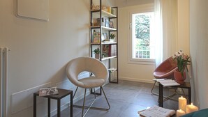Un soggiorno moderno con una poltrona rotonda, una libreria, un tavolino con candele e una finestra con tende.