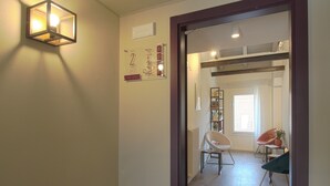 Un corridoio con un punto luce a parete, un telaio di porta e uno scorcio di una stanza con una sedia e un tavolo.