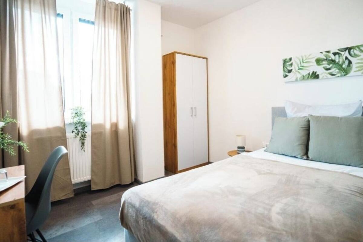 A hotel room with a bed, a desk, a chair, a wardrobe, and a window with curtains.