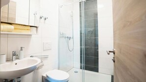A bathroom with a white sink, toilet, and glass-enclosed shower. - Hotel am Schafbaum (Bad Rappenau)