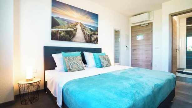 A bedroom with a bed, a nightstand, a painting, and a door. - Hotel am Schafbaum (Bad Rappenau)