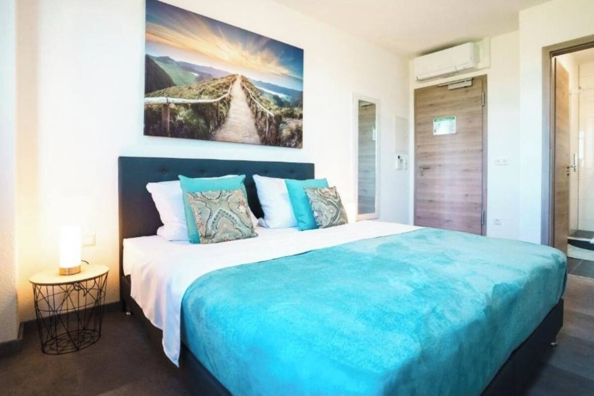 A bedroom with a bed, a nightstand, a painting, and a door.