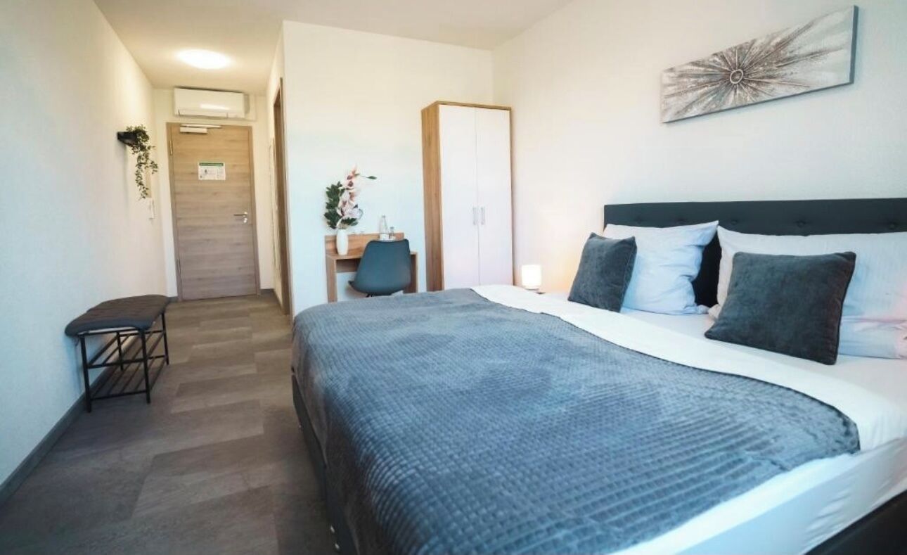 Une chambre d’hôtel comprenant un lit, une table de chevet, une chaise et un bureau avec une autre chaise.