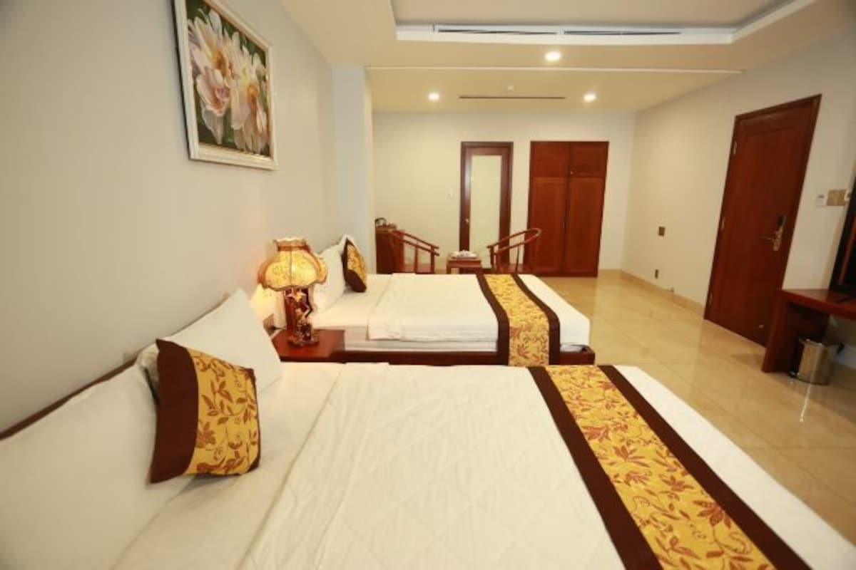 A hotel room with two beds, a desk, a chair, a lamp, and a painting on the wall.