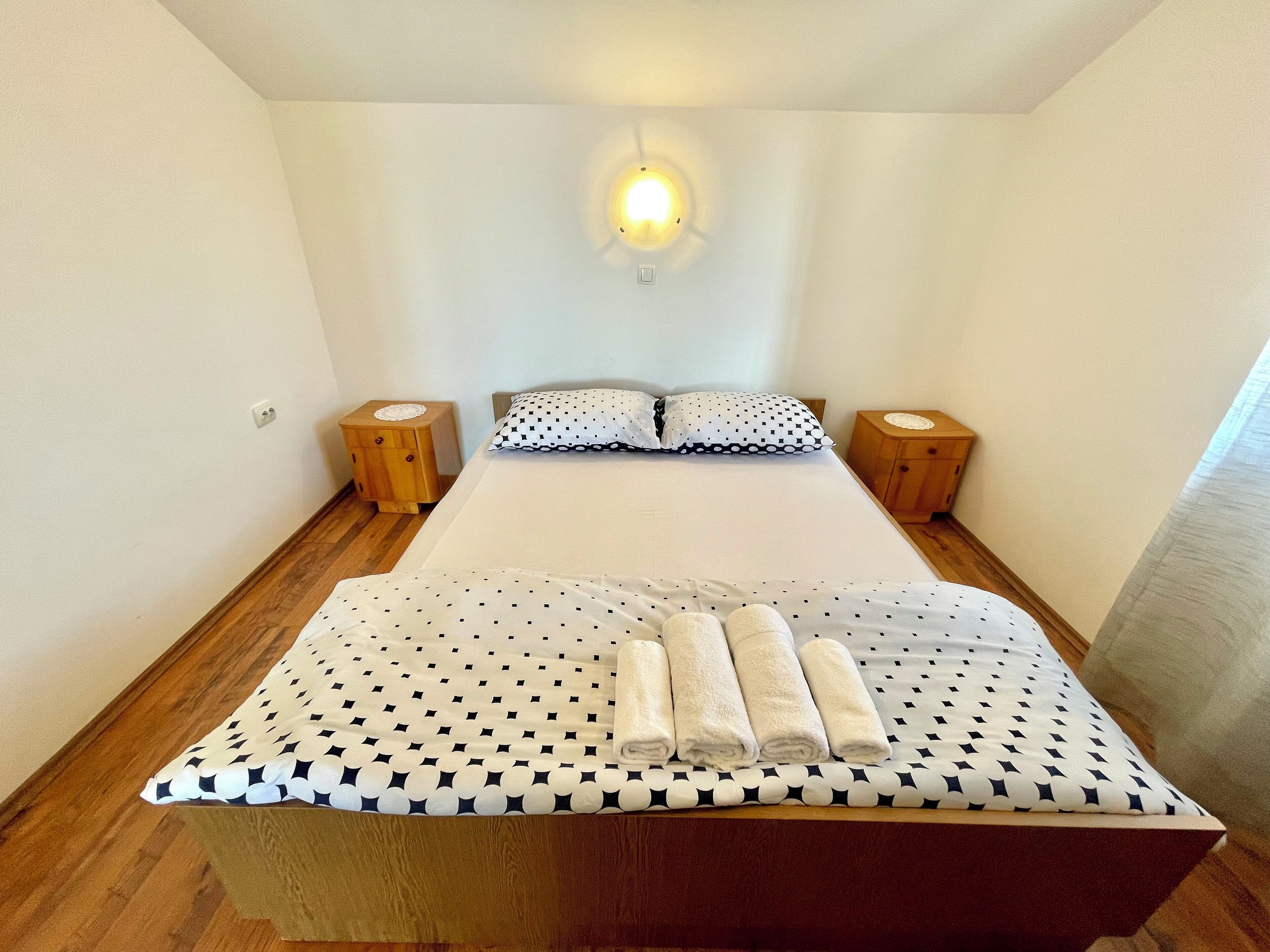 A neatly made bed with a checkered bedspread and pillows, two bedside tables, and a wall-mounted light fixture.