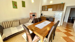 Un espacio habitable compacto con mesa de comedor, sofá, zona de cocina y un refrigerador pequeño.