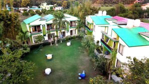 A residential area with multiple two-story houses, each with a green roof and white walls. There are several outdoor seating areas with tables and chairs. - De Floresta resort (Ramnagar)