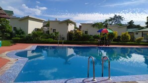 A swimming pool with a tiled edge, surrounded by buildings and greenery. - De Floresta resort (Ramnagar)