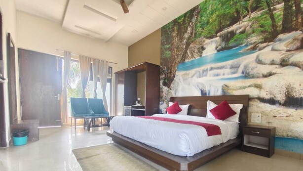 A spacious bedroom with a large bed, a mural of a waterfall, and a view of the outdoors. - De Floresta resort (Ramnagar)