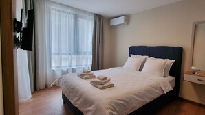 A hotel room with a bed, a large mirror, a window with sheer curtains, and an air conditioning unit.