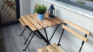 A wooden table with benches, a potted plant, and a lantern on a balcony with a view of the street.