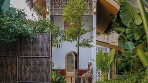 Une structure traditionnelle en bambou, surmontée d’un toit de chaume, entourée d’une végétation luxuriante et agrémentée d’un petit étang où nagent des carpes koï.