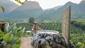Une personne assise au bord d’un jacuzzi, avec un paysage montagneux en arrière-plan.