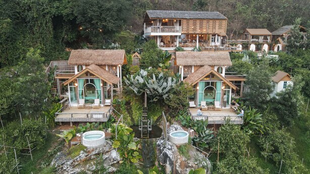 Un complexe hôtelier composé de plusieurs bâtiments de style bungalow, chacun doté d’un toit de chaume, d’un espace salon extérieur et d’une piscine.