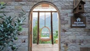 Une chaise suspendue en bois, placée dans un passage en arc de cercle, offre une vue sur la verdure et les montagnes.