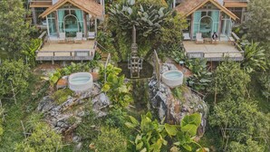 Un complexe hôtelier comprenant plusieurs bungalows aux toits de chaume, chacun doté d’un balcon et entouré d’une végétation luxuriante.