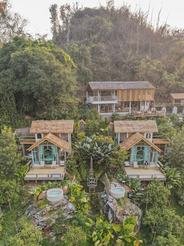 Un complexe hôtelier comprenant plusieurs bungalows aux toits de chaume, chacun doté d’un balcon et entouré d’une végétation luxuriante.