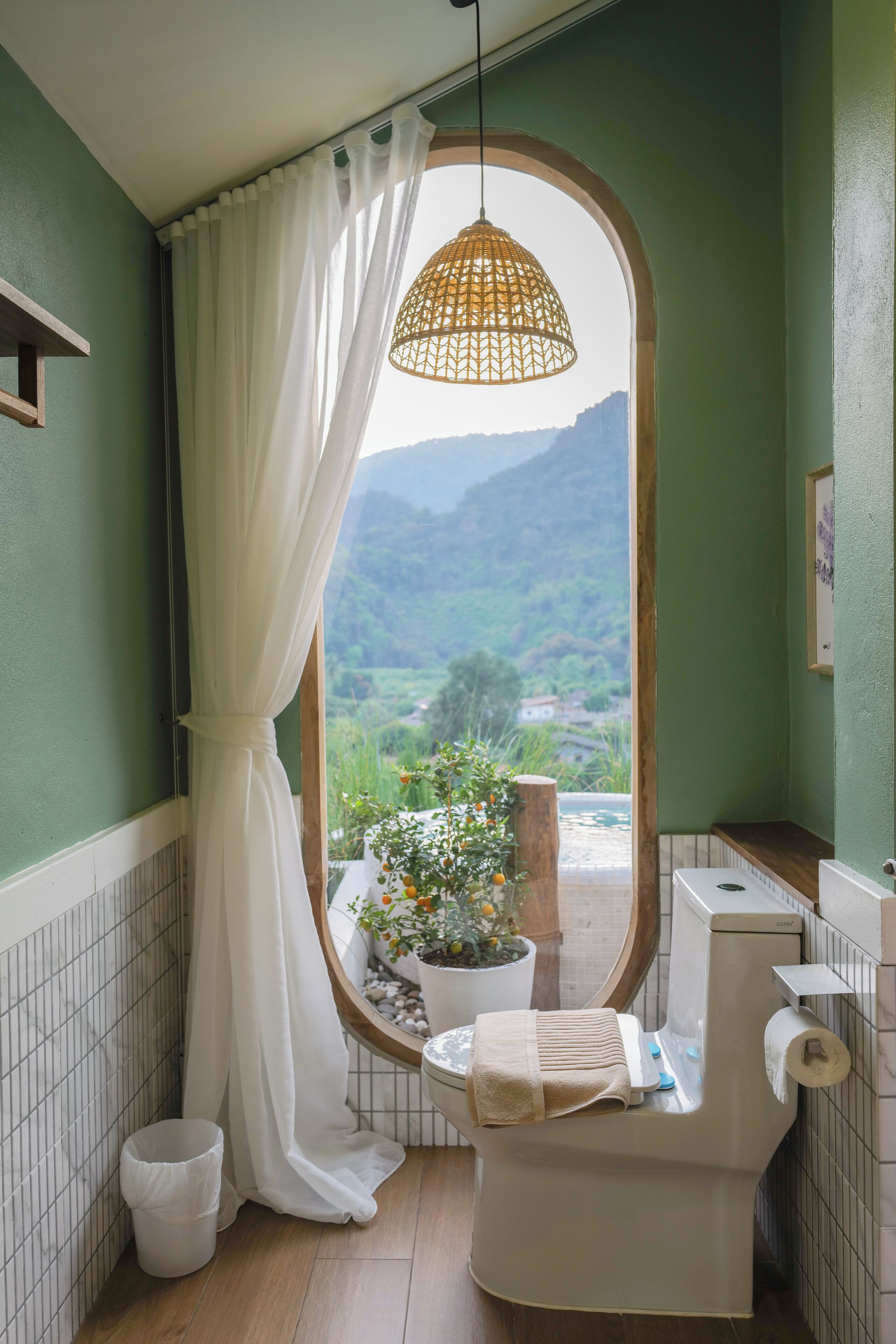 A bathroom with a view of a mountainous landscape through a window, a hanging light fixture, and a toilet with a towel on it.