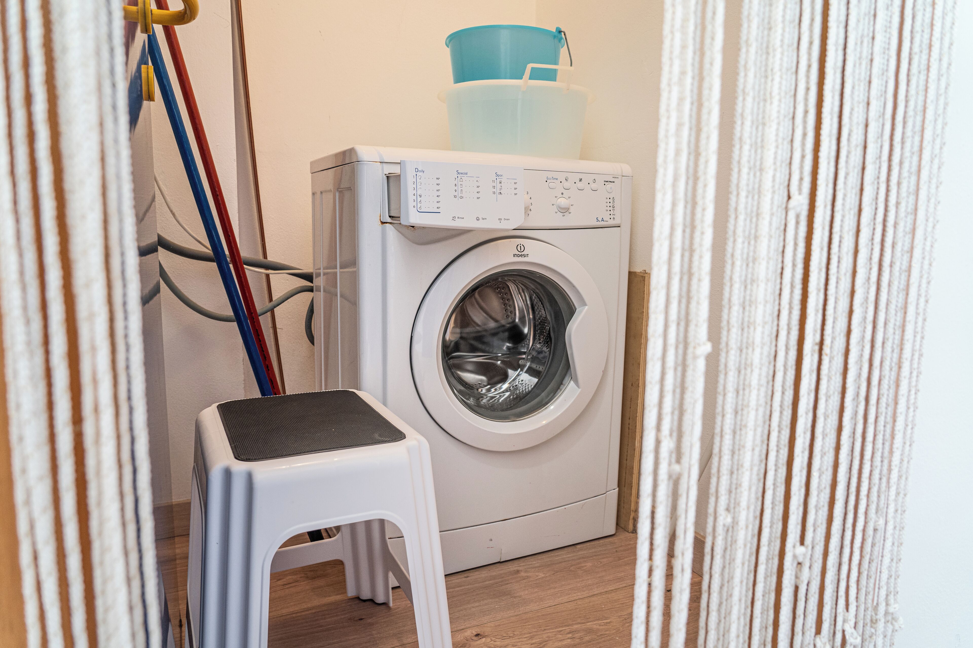 Une machine à laver à chargement frontal, dotée d’un panneau de commande, d’un tabouret en plastique et d’un seau bleu posé sur le dessus.