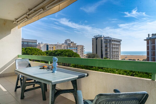 A balcony with a table and chairs, overlooking a beach and buildings.