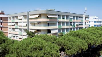 A multi-story building with balconies, surrounded by dense green trees.